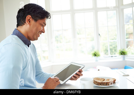 Indian Man Using Digital Tablet Whilst Eating Breakfast Stock Photo
