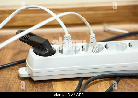 Many plugs plugged into electric power bar on office floor Stock Photo