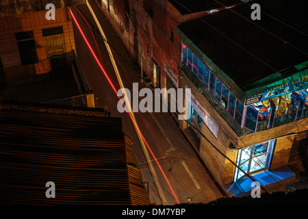 Lights zigzag past a closed cafe through the quiet night streets of Agra's Taj Ganj district in this long exposure photograph. Stock Photo