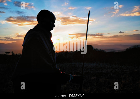 Silhouetted Maasai warrior holding a spear at the plains of the Ngorongoro Conservation Area in the Crater Highlands area of Tanzania Eastern Africa Stock Photo