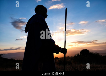 Silhouetted Maasai warrior holding a spear at the plains of the Ngorongoro Conservation Area in the Crater Highlands area of Tanzania Eastern Africa Stock Photo