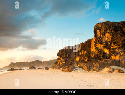 Large sea cliffs at sunrise with white sand and two motion blurred people fishing Stock Photo