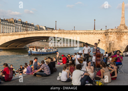 YOUTHS RELAXING BY THE SEINE ON THE QUAY DE LA TOURNELLE, WITH A HOUSEBOAT AND THE LA TOURNELLE BRIDGE, PARIS (75), FRANCE Stock Photo