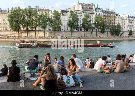 YOUTHS RELAXING BY THE SEINE ON THE QUAY DE LA TOURNELLE, WITH A HOUSEBOAT ON THE RIVER, PARIS (75), FRANCE Stock Photo