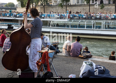 YOUTHS RELAXING WITH MUSIC (DOUBLE BASS) BY THE SEINE ON THE QUAY DE LA TOURNELLE, WITH A HOUSEBOAT AND THE LA TOURNELLE BRIDGE, PARIS (75), FRANCE Stock Photo