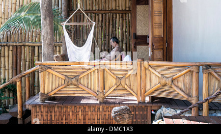 tourist sitting on balcony peering at his mobile phone & enjoying the good life in luxury beach hotel with rustic chic ambiance Stock Photo