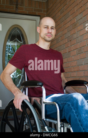 Disabled man suffering from an illness sits in his wheelchair in front of his home. Stock Photo