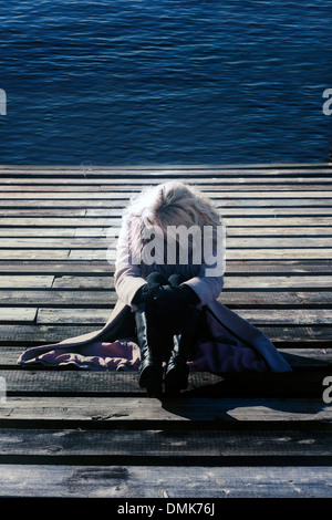 a blond girl in a pink coat is sitting on a wooden footbridge Stock Photo