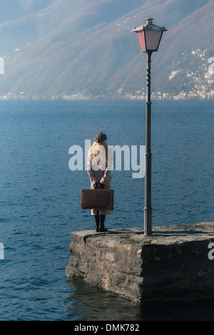 a woman in a pink coat is standing on a jetty at a lake Stock Photo