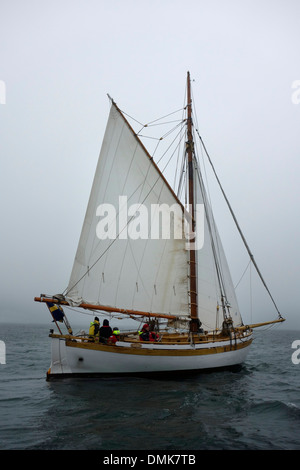 Gaff rigged sloop with sails on starboard tack sails into dense fog Stock Photo