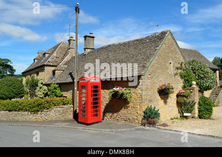 Honey coloured stone houses and a red telephone box in a village in the Cotswolds in rural England. Stock Photo