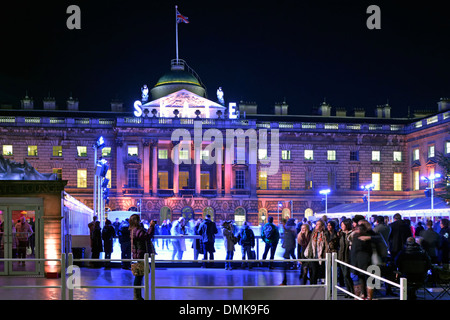 People watch ice skaters Somerset House night floodlit facade of historical building around temporary winter ice skating rink in courtyard London UK