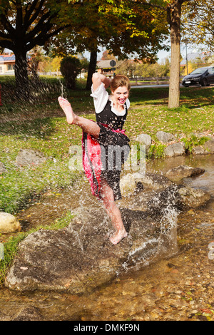 Young woman in a dirndl playing in a stream Stock Photo