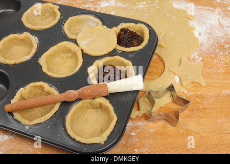 Preparing mince pies, rolled sweet pastry and mince pie ingredients in a baking tray on a wooden worktop Stock Photo