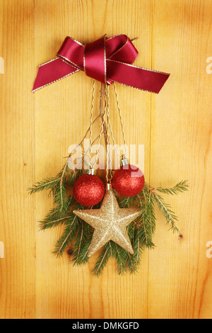 Christmas decoration of a red bow, Christmas tree branch and baubles hanging on a wooden panel