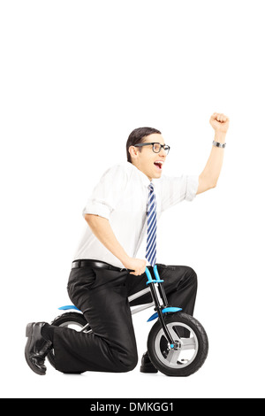 Excited young businessperson riding a small bicycle and gesturing happiness with his hand Stock Photo