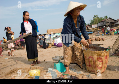 A woman is preparing to weigh fish on a scale at a transportation waypoint busy with activity near Pakse, Southern Laos. Stock Photo