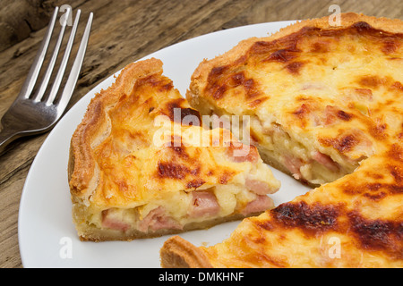 Portion of cheese and bacon flan cut from the quiche lorraine in a rustic traditional farmhouse setting Stock Photo
