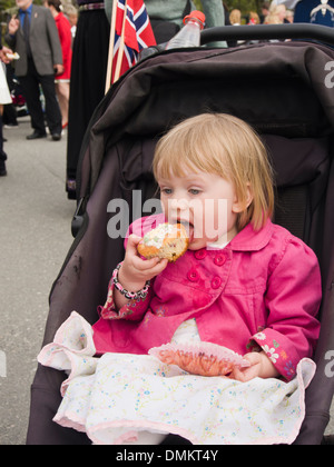 Toddler girl  in pram eating a muffin, pretty in pink, Nesodden Oslo Norway Stock Photo