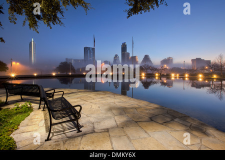 A bench on the side of a reflecting pool offers a great view of downtown and the Austin skyline on a foggy morning. Stock Photo