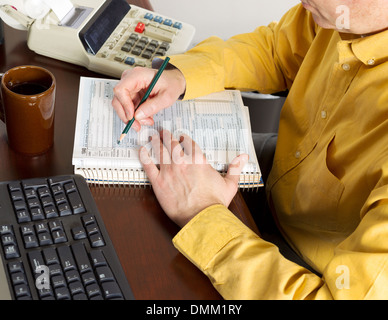 Horizontal photo of mature man, partial face view, working on his taxes with calculator, tax tables and other office equipment Stock Photo