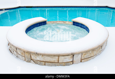 Outdoor residential hot tub or spa by swimming pool surrounded by snow in the winter Stock Photo