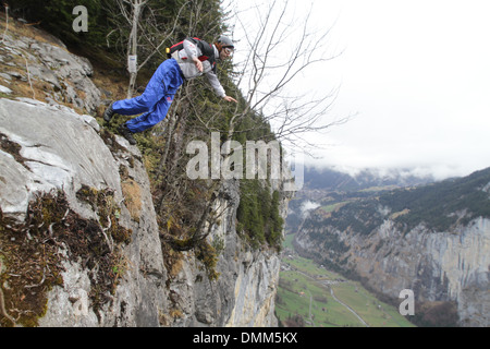 BASE jumper is exiting from a cliff down into the deep valley. He is jumping forward away from the rock. Stock Photo