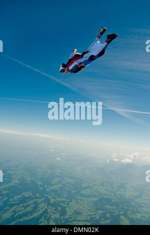 Skydiver is flying in his Wingsuit and is diving down from the blue sky direction earth with high speed. Stock Photo