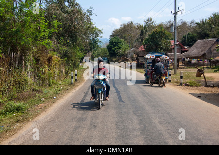 Horizontal portrait of two local Lao guys riding a motorbike along the road without helmets in the Laos countryside. Stock Photo