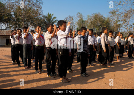 Horizontal view of school children saluting and singing together during their flag raising at a school in Laos. Stock Photo