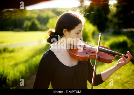 Profile in artistry: pretty young brunette woman strikes just the right note on her antique italian violin; oh, and sunlight! Stock Photo