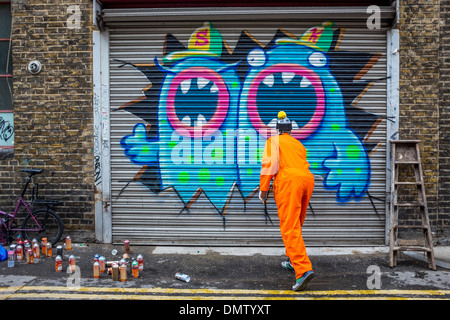 Street artist, Ronzo, at work. Artist uses spray paints to paint giant graffiti monster on a door - Fashion Street, London, UK Stock Photo