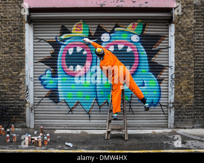 Street artist, Ronzo, at work. Artist uses spray paints to paint giant graffiti monsters on a wall - Fashion Street, London, UK Stock Photo