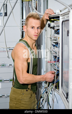 Handsome male electrician in front of power panel, looking at camera Stock Photo