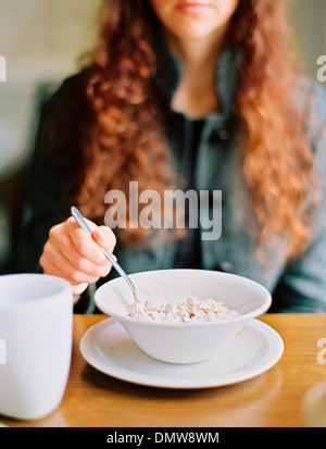 A woman eating breakfast cereal from a white bowl. Stock Photo