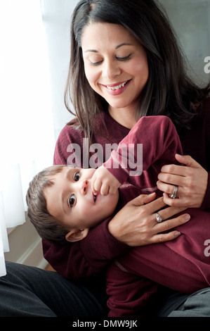 A beautiful Hispanic woman holds her playful son, smiling. A multiracial mother and son family portrait. Stock Photo