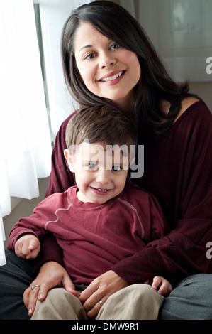 A beautiful Hispanic woman holds her playful son, smiling, pointing finger. A multiracial mother and son family portrait. Stock Photo