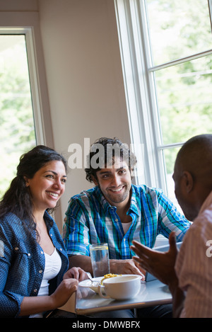 Three people seated at a cafe table talking. Stock Photo