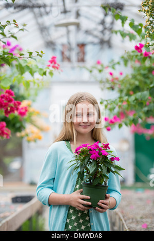 An organic flower plant nursery. A young girl holding a flowering plant. Stock Photo