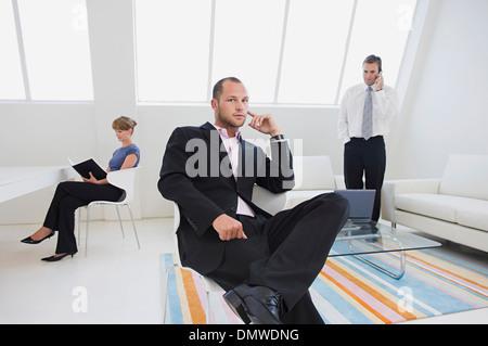 Three business people in an office one on  phone one working on a digital table and one seated in a chair. Stock Photo