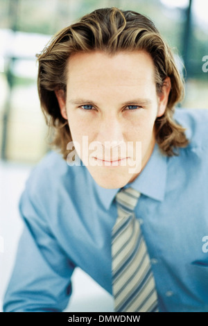 A young man with curly brown hair wearing a blue shirt and tie. Stock Photo