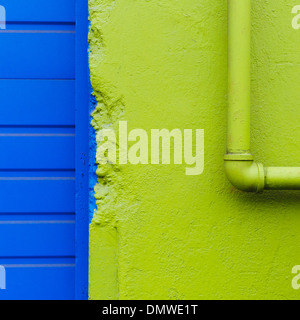 A green painted wall and pipe by a blue doorway. Stock Photo
