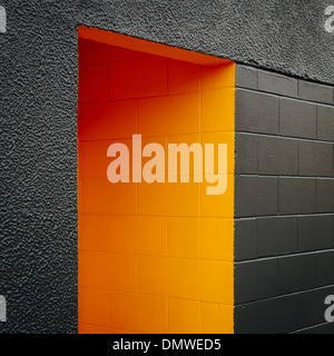 A doorway recess painted orange in a grey block concrete wall. Stock Photo