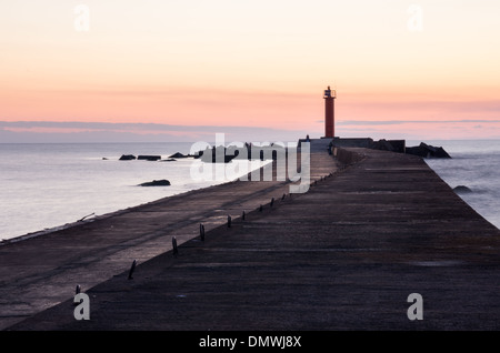 A colourful after sunset scene by the sea. River Daugava flows into Riga bay of Baltic sea. Concrete mole and lighthouse. Stock Photo