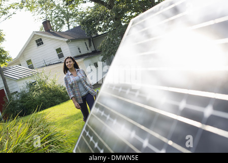 A woman walking towards a solar panel in a farmhouse garden. Stock Photo