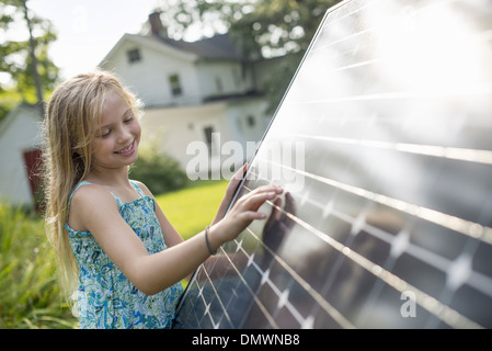 A young girl beside a large solar panel in a farmhouse garden. Stock Photo