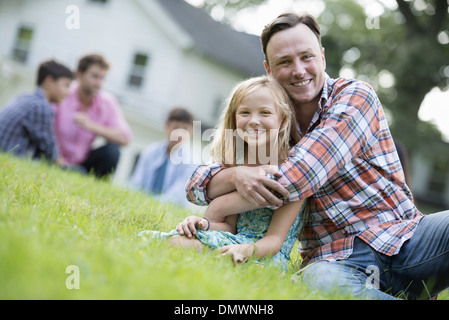 A father and daughter at a summer party sitting on  grass. Stock Photo