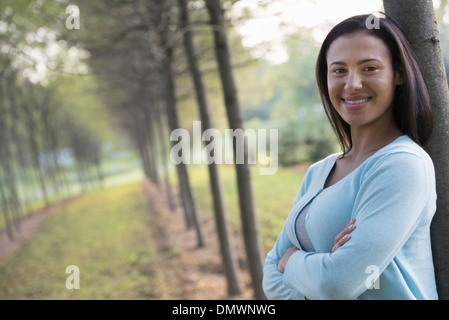 A woman with arms folded leaning against a tree.