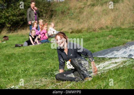 Woman sliding down a water slide being watched by a group of children in the background during Endurance race Derbyshire Stock Photo