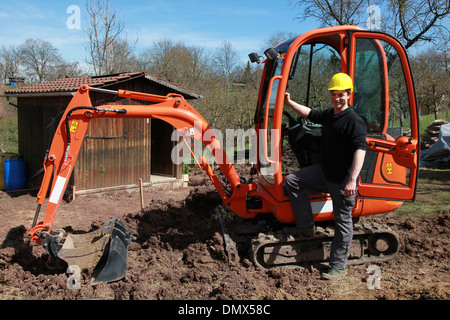 Young worker in front of an excavator in a garden Stock Photo